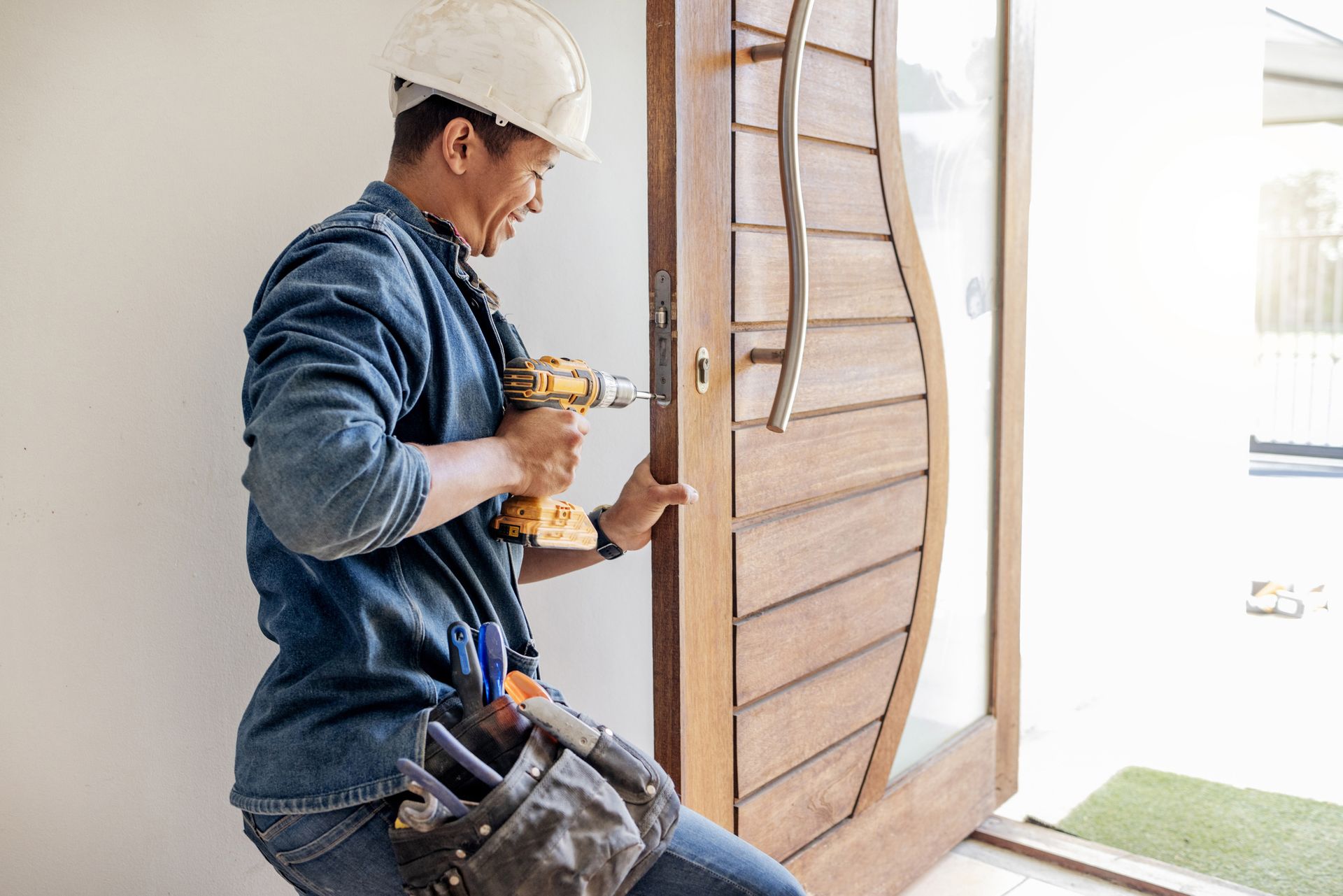 A door installation contractor, in a blue uniform and a white helmet, finishing the installation.