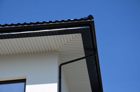 A white house with a black gutter and a blue sky in the background.