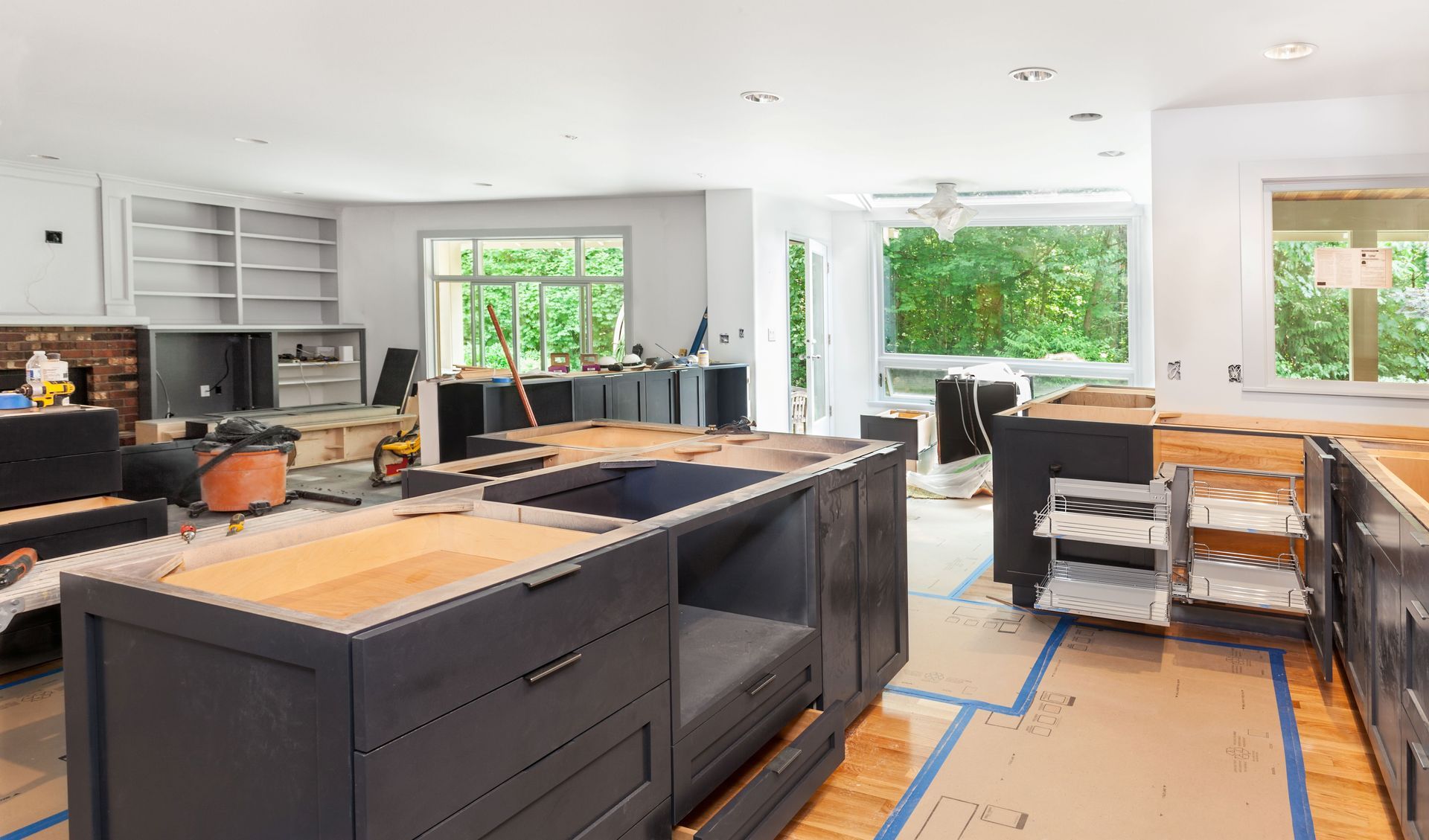 Bright modern kitchen under renovation with black cabinets, wood countertops, and taped floor protection