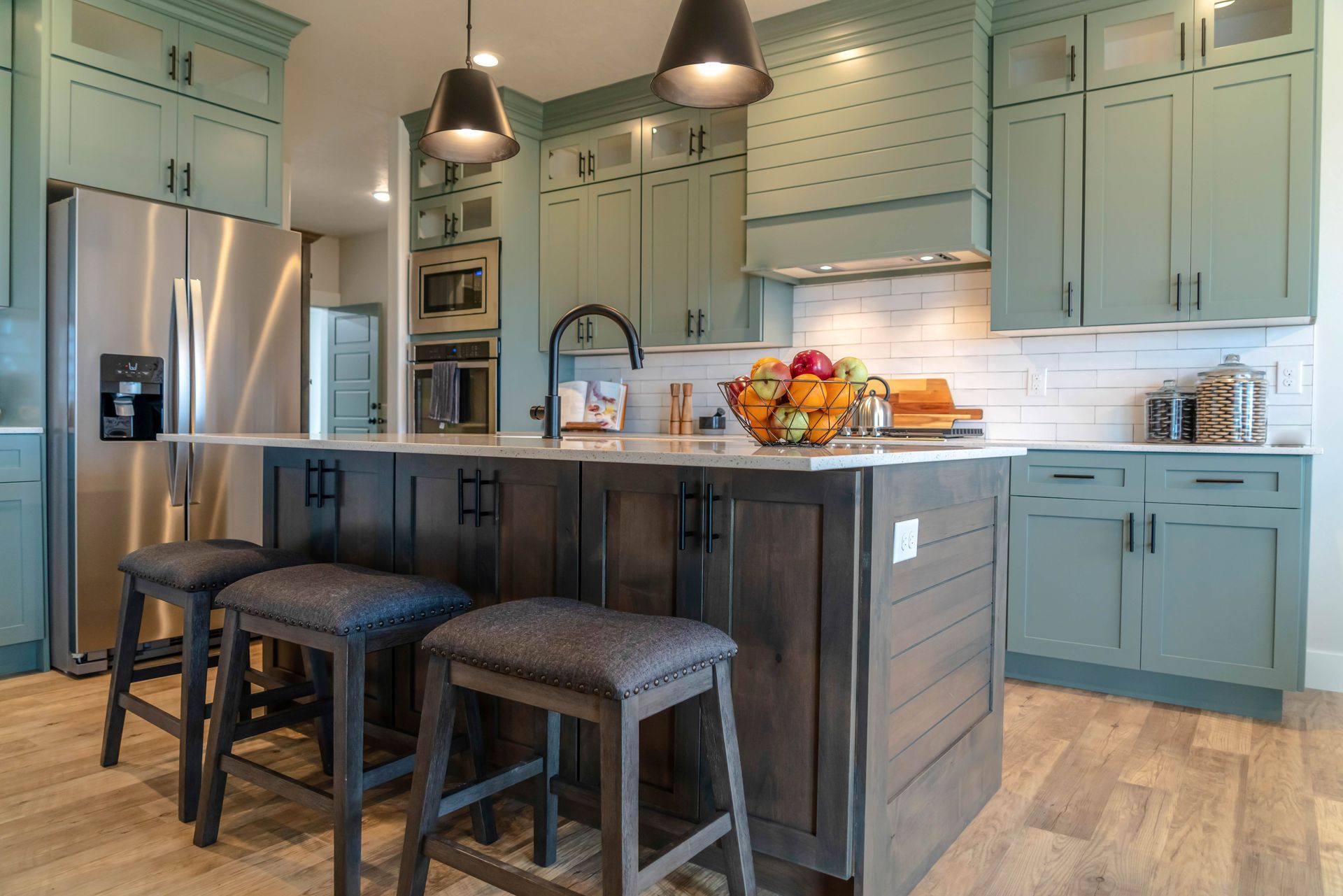 Mint-green kitchen with dark wood island, barstools, hanging lights, and a fruit bowl on the counter