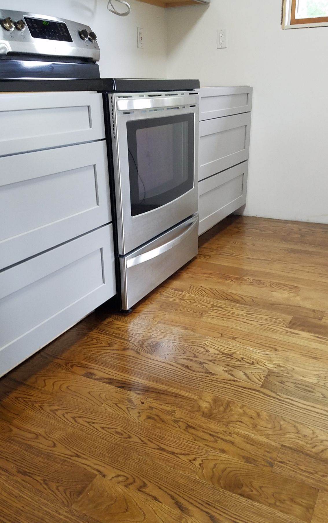A light-colored hardwood floor featuring a rectangular wooden air vent, situated next to a white wall baseboard.