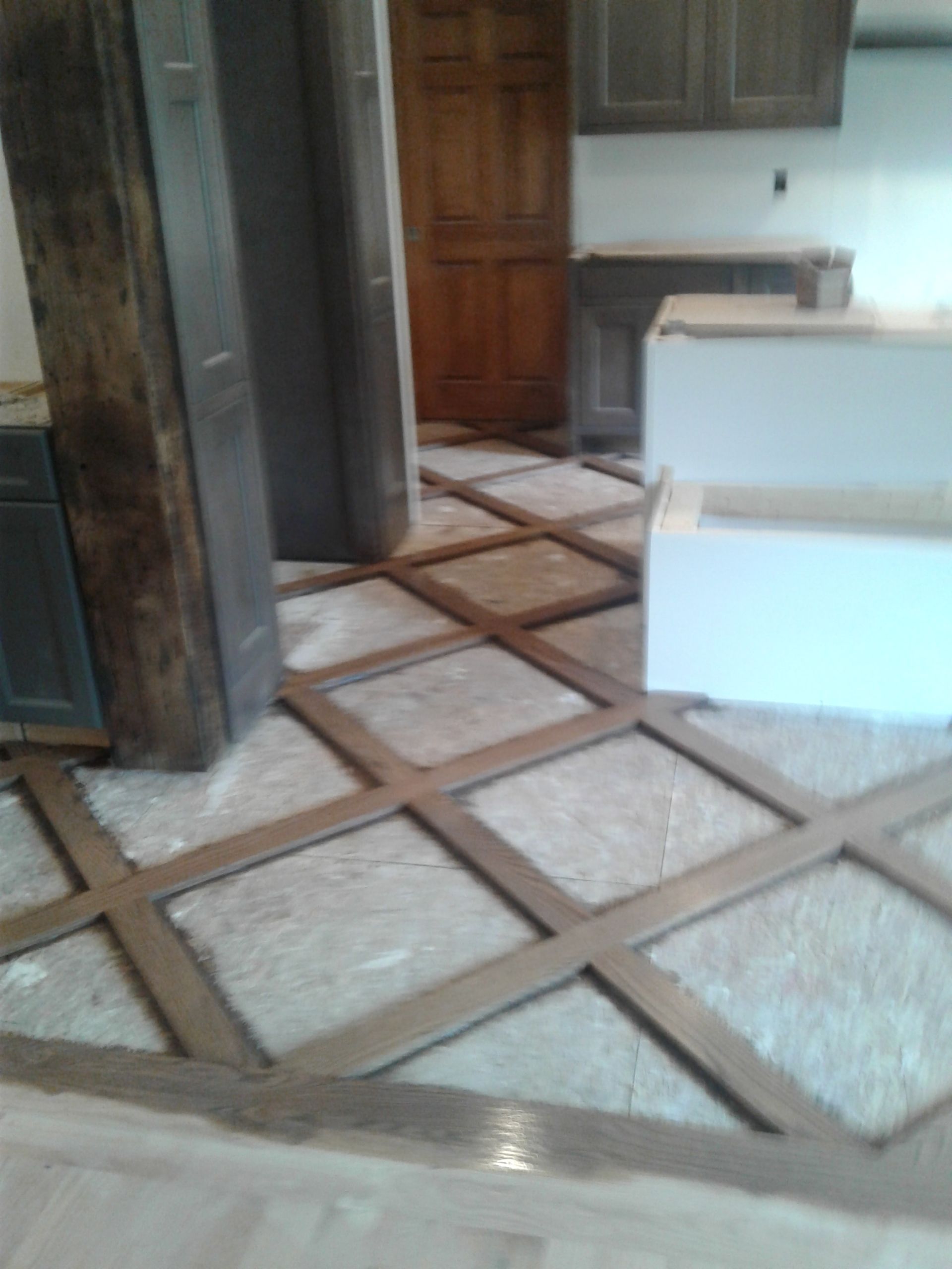 A room under construction with a diamond-pattern wood frame on the floor and unfinished kitchen cabinetry in the back.