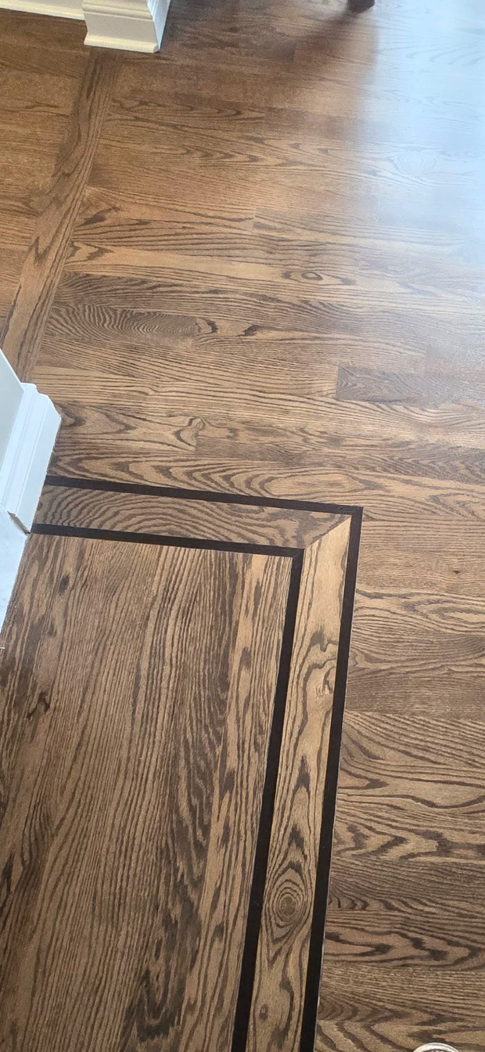 A high-angle view of brown oak hardwood flooring featuring a dark wood inlay border detail.