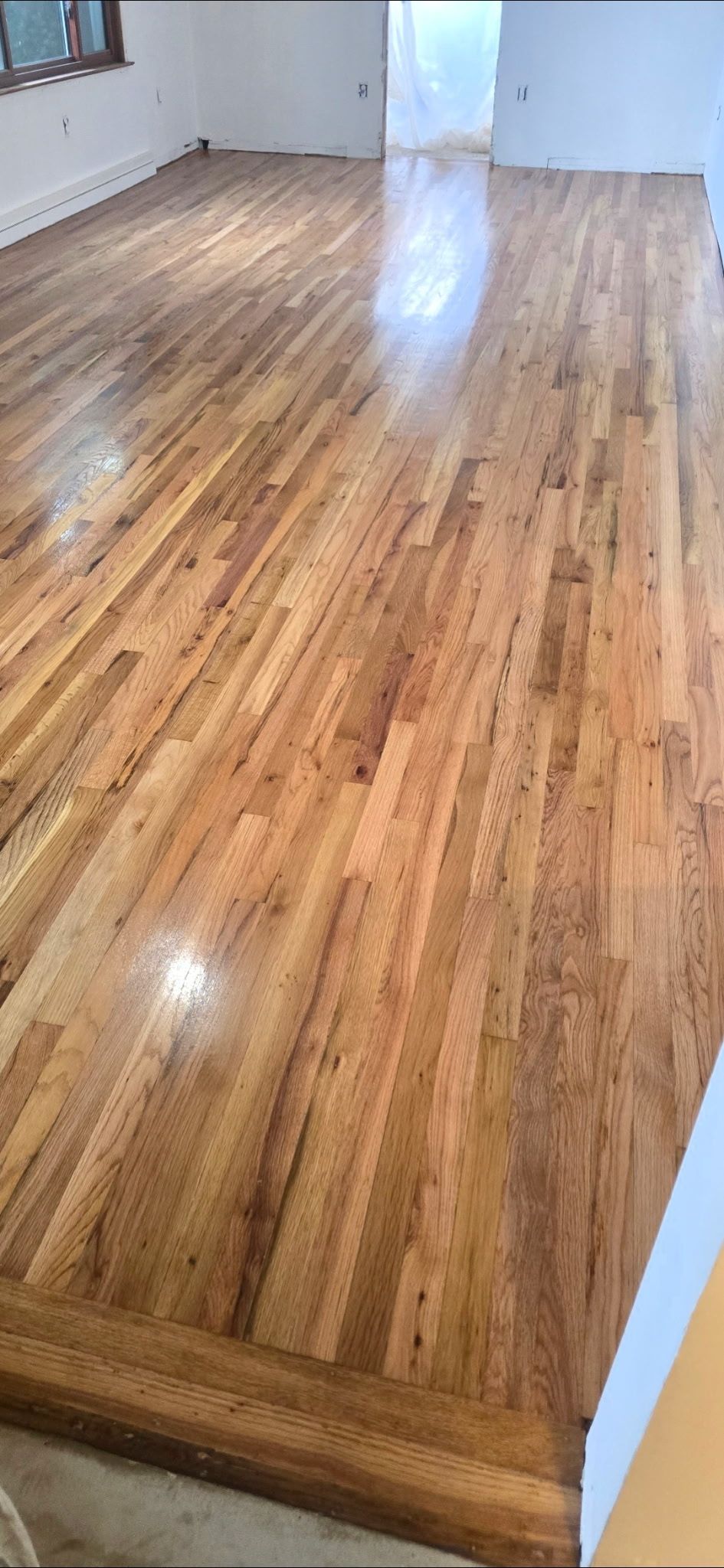 A high-angle view of freshly refinished, light brown hardwood flooring extending across a bright, empty room.