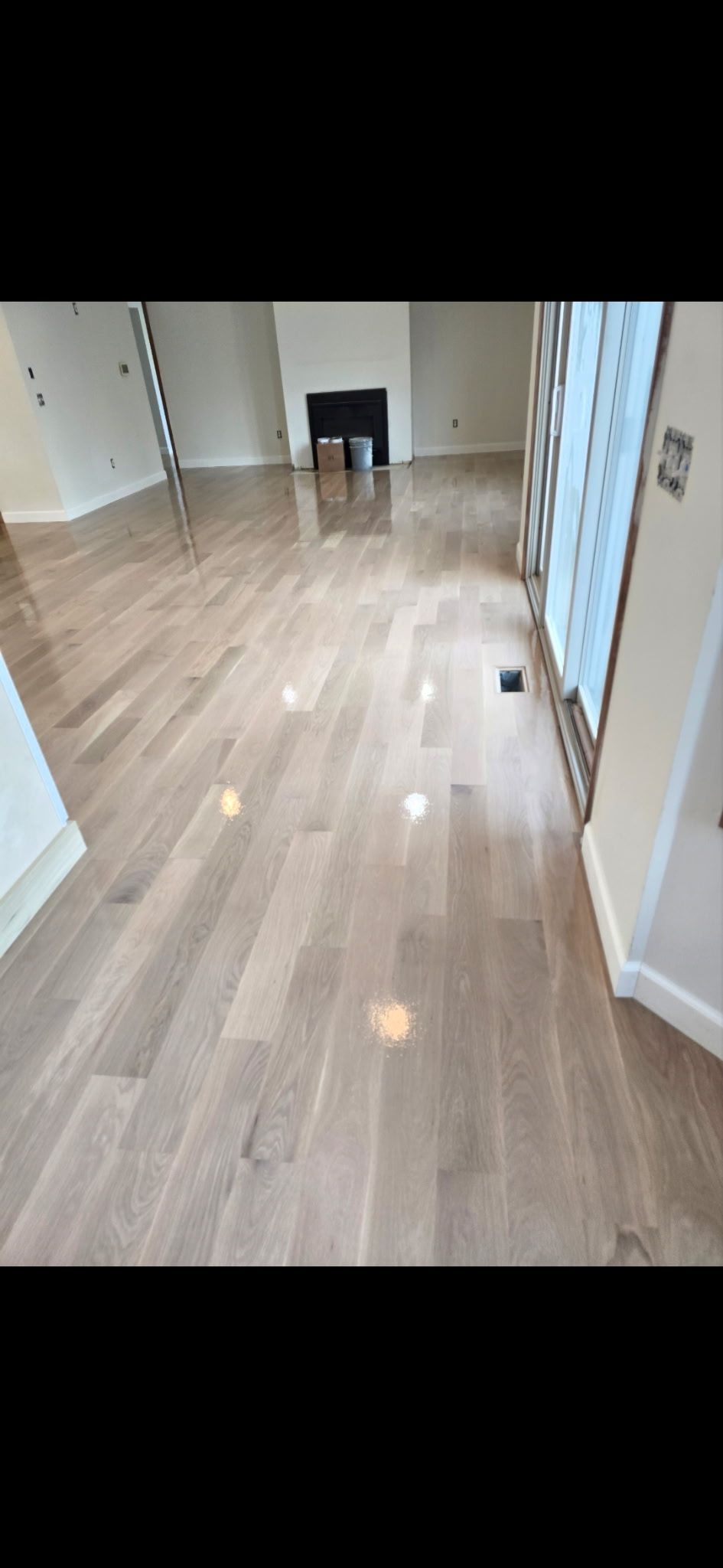 Light-colored hardwood flooring in a room with white walls, recessed lighting, and a fireplace in the background.