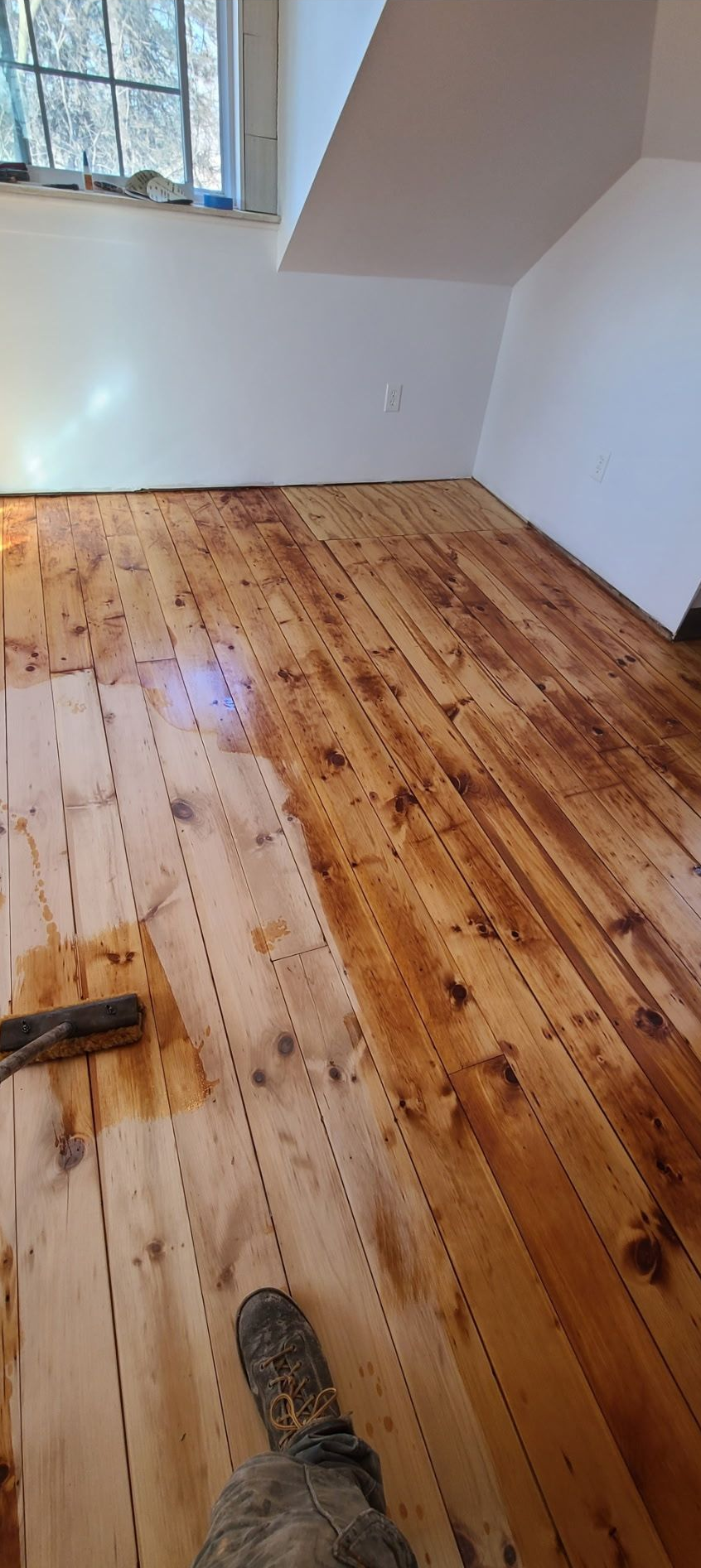 A light-colored hardwood floor featuring a rectangular wooden air vent, situated next to a white wall baseboard.