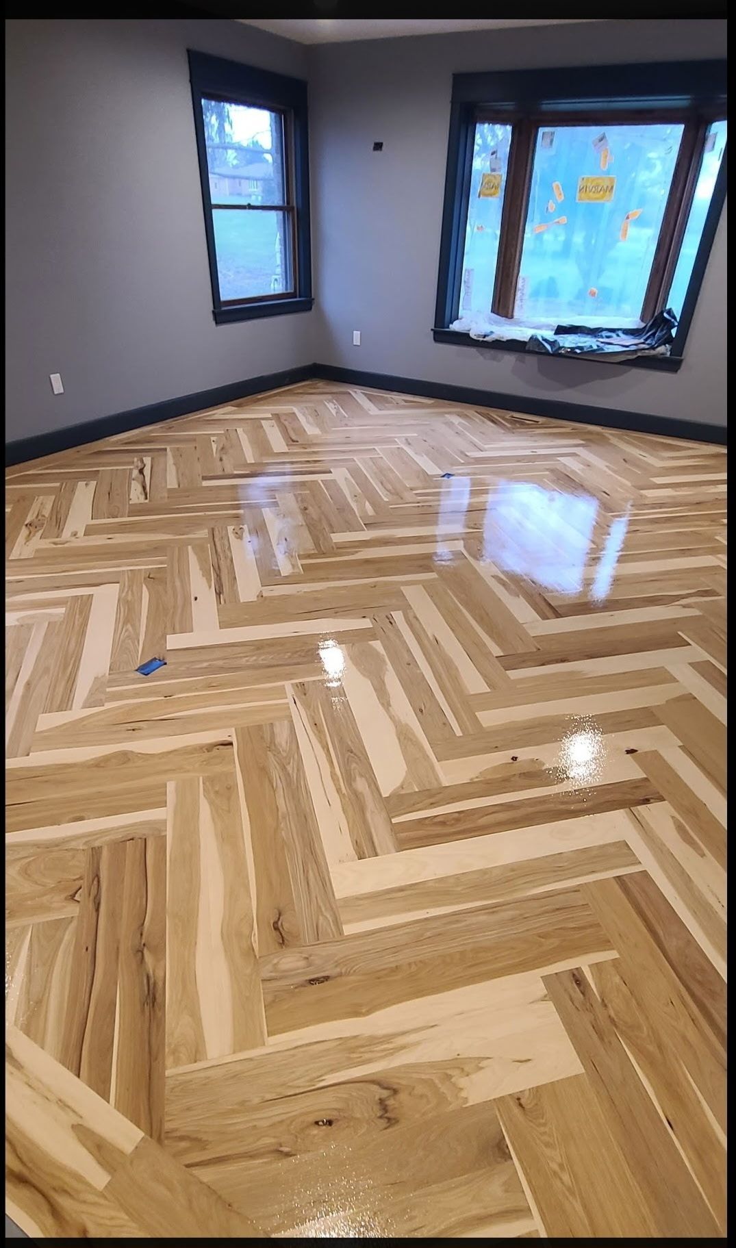 A room with gray walls, dark trim, and a high-gloss herringbone wood floor with varying shades of natural wood grain.