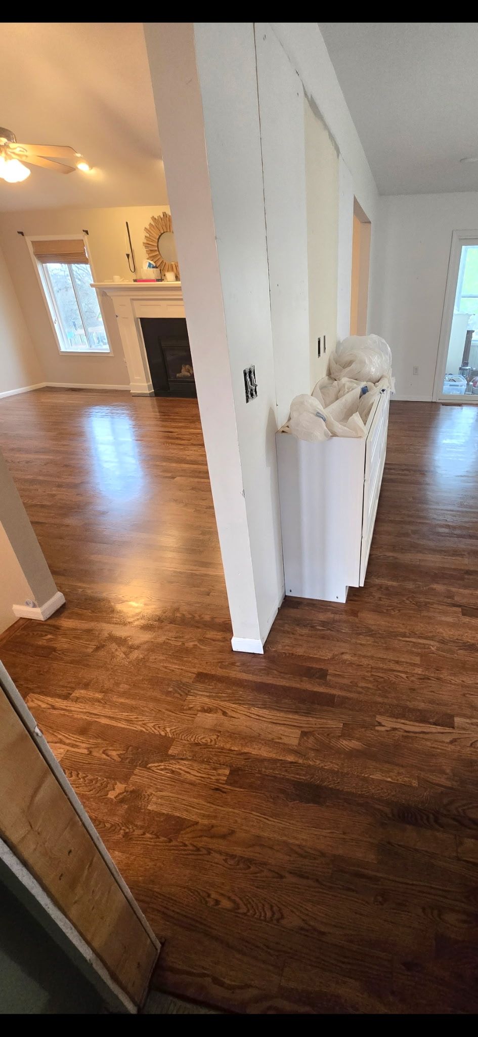 A view of an open-concept home interior with dark hardwood floors, white walls, and a fireplace in the background.