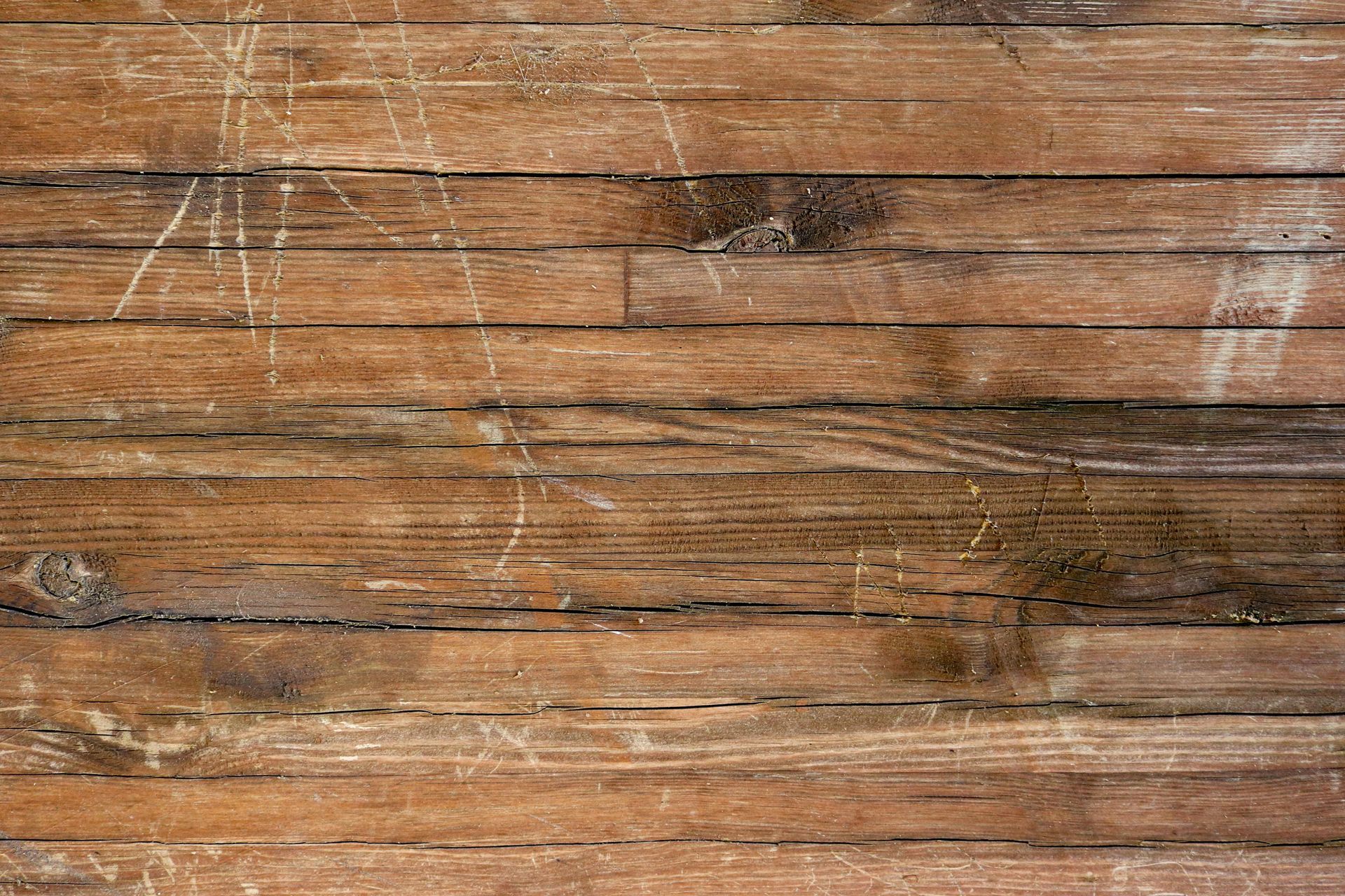 A person installs light-colored hardwood flooring in a room under construction with bare walls and tools scattered around.