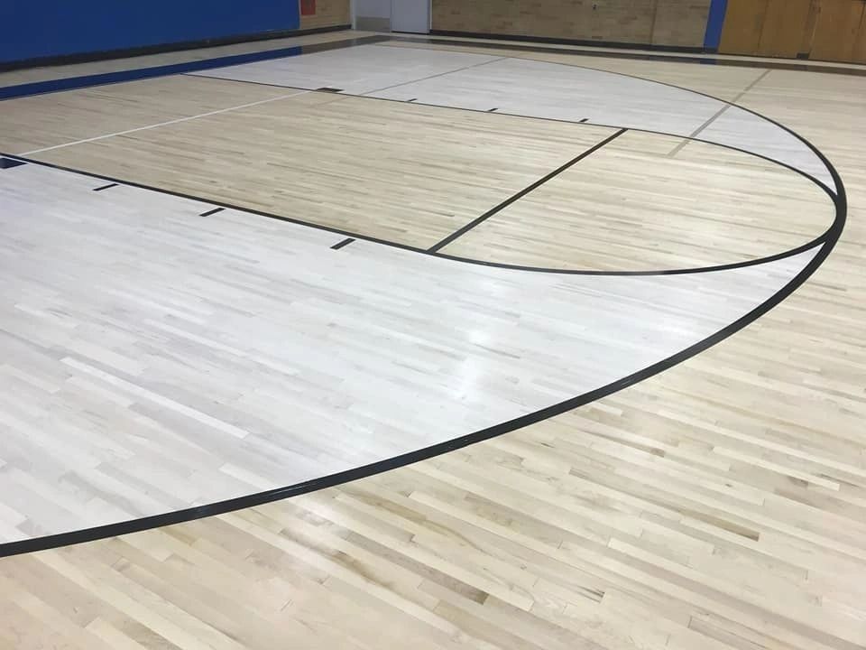 A basketball court section showing a white-painted key and three-point arc on light-colored wooden flooring.