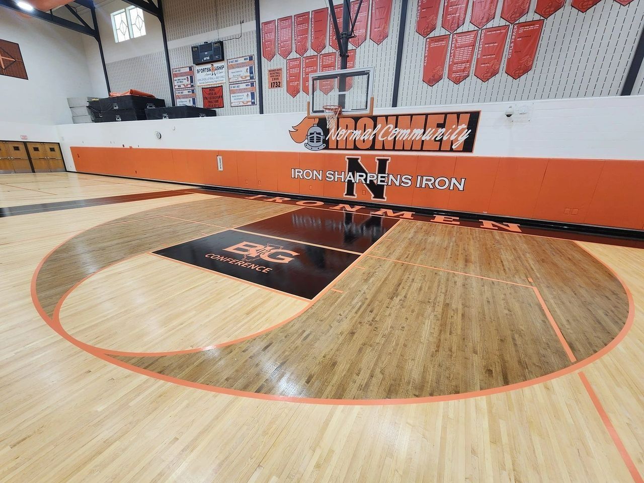 An indoor basketball court with a dark-stained key area, orange markings, and wall signage reading 