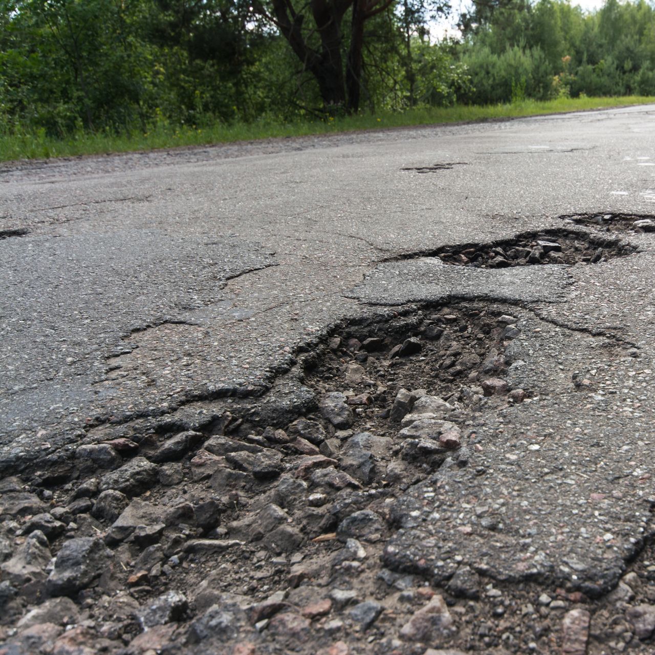 A road with holes in it and trees in the background