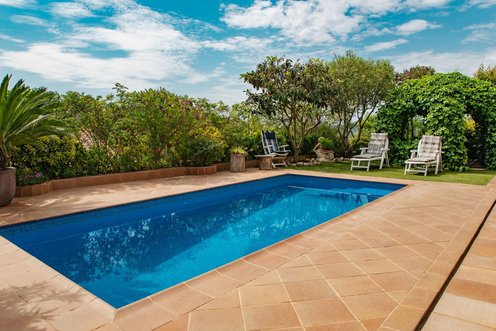 A large swimming pool surrounded by lawn chairs and trees.