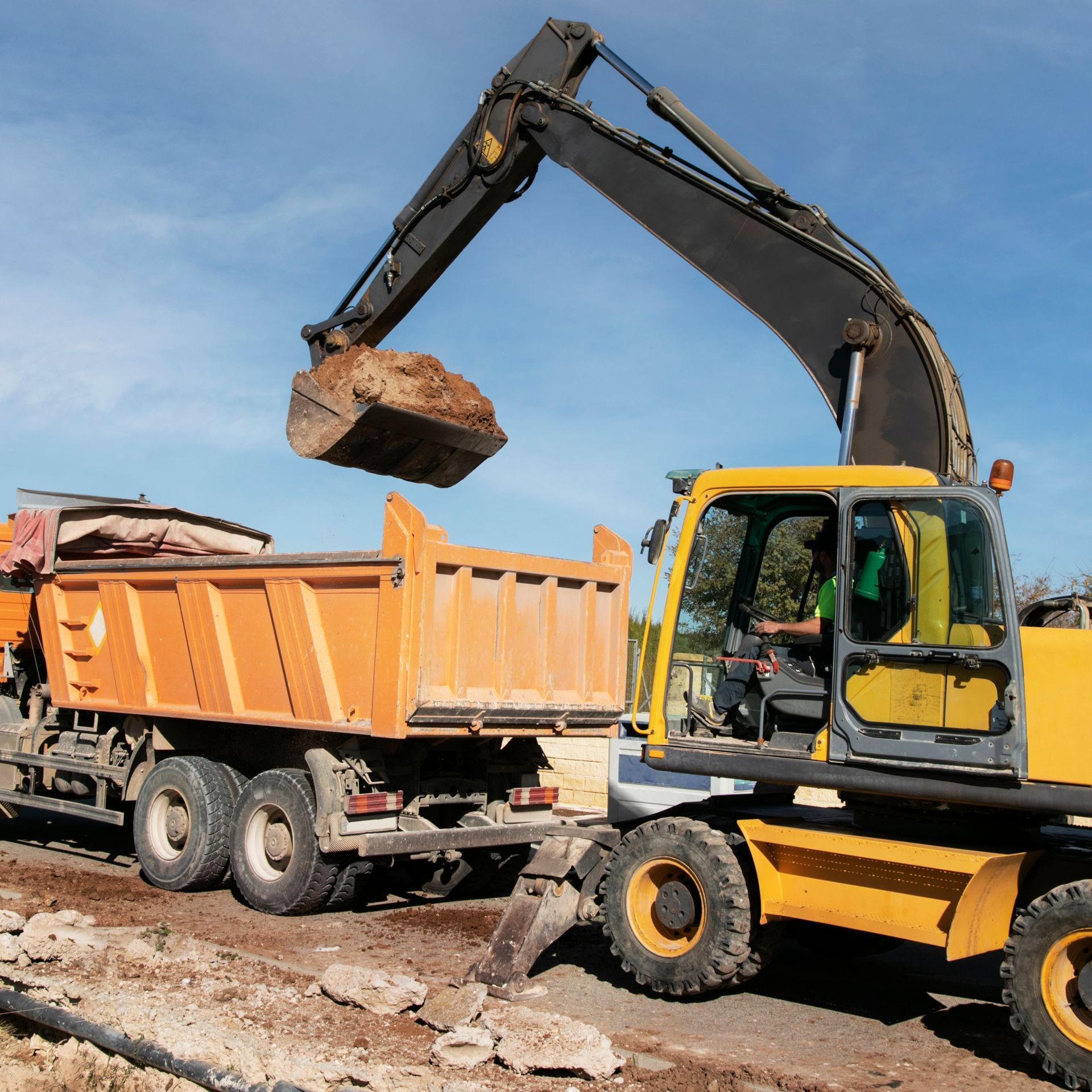 An excavator is loading dirt into an orange dump truck