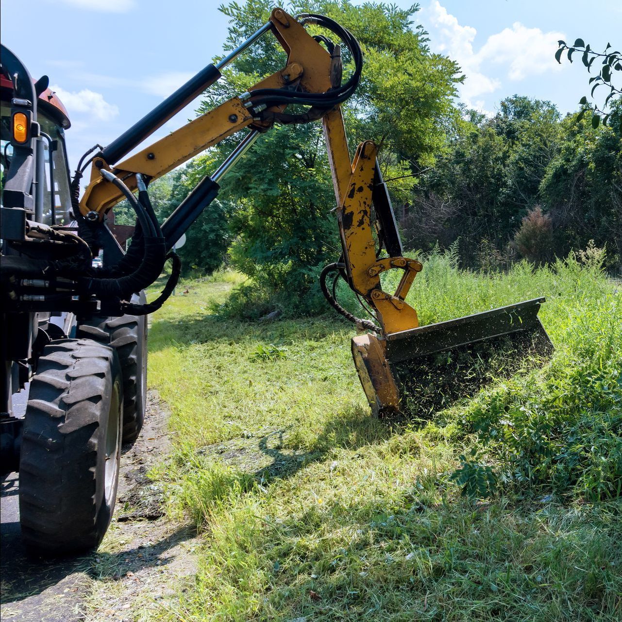 A tractor is cutting grass in a field with trees in the background