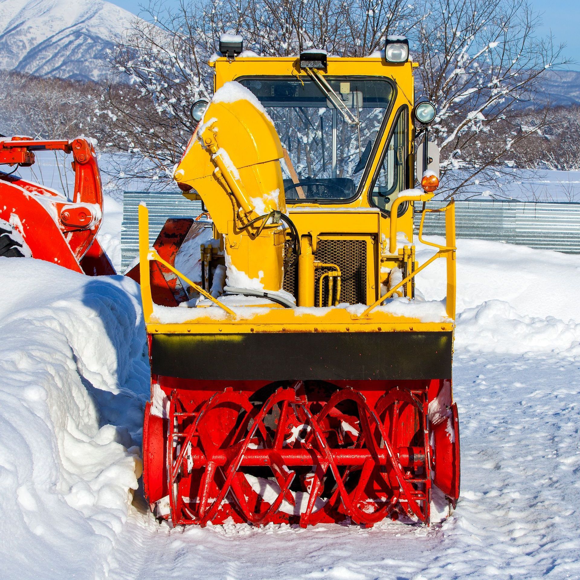 A yellow and red snow blower in the snow