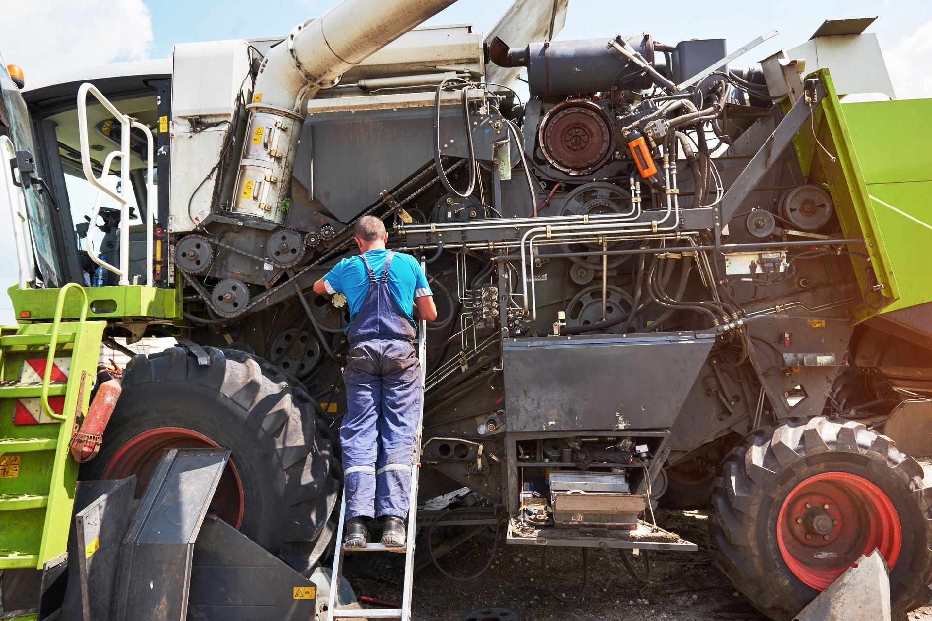 A man is standing on a ladder working on a combine harvester.