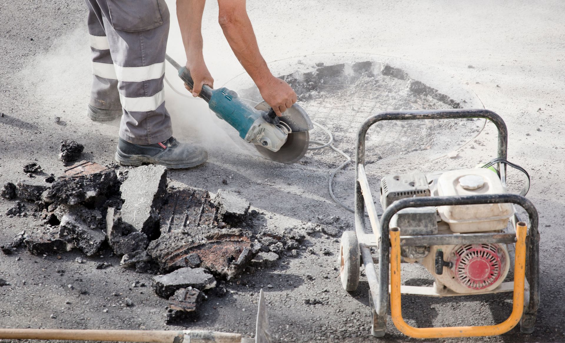 A man is using a grinder to cut a hole in the ground.