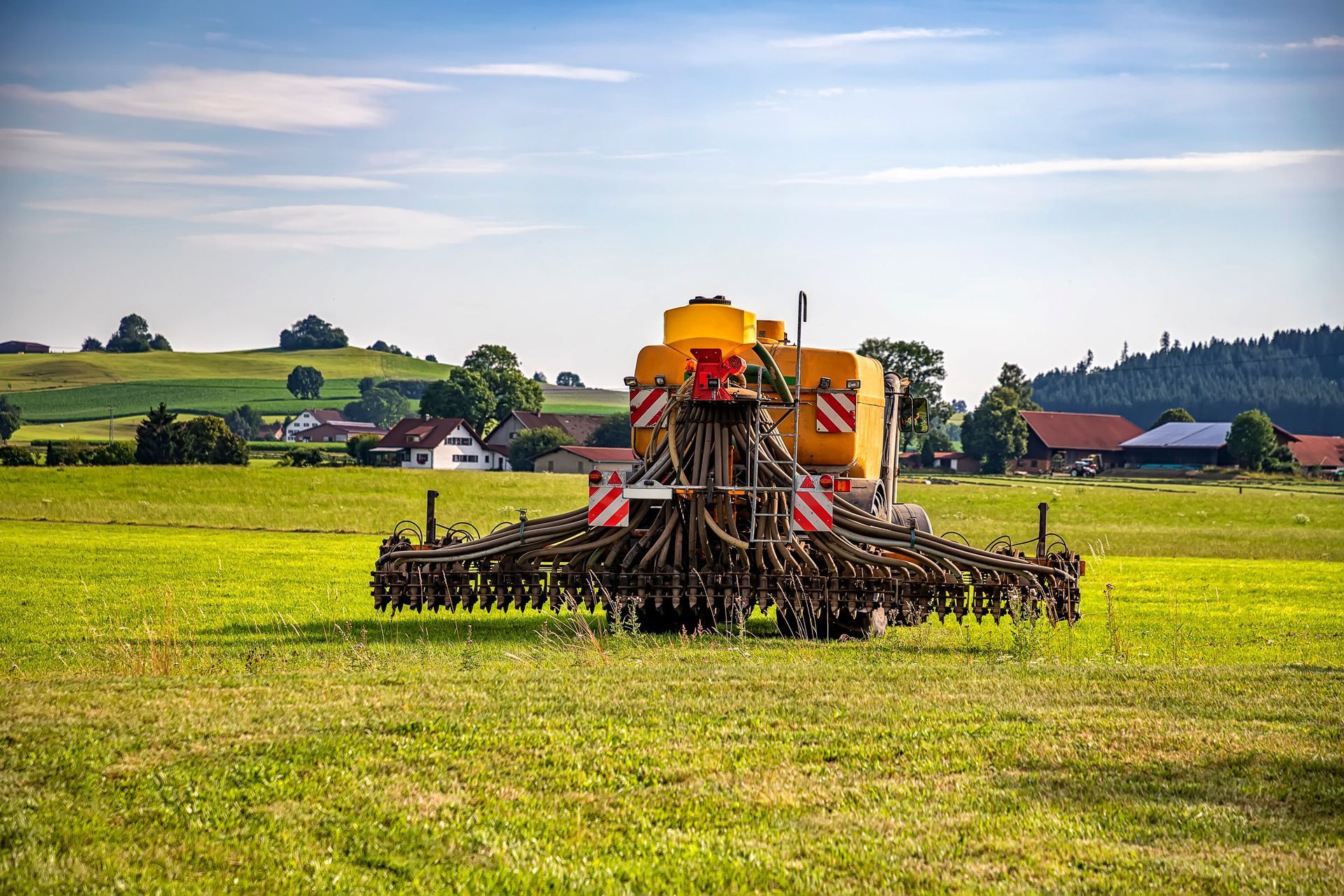 A yellow tractor is plowing a field of grass.