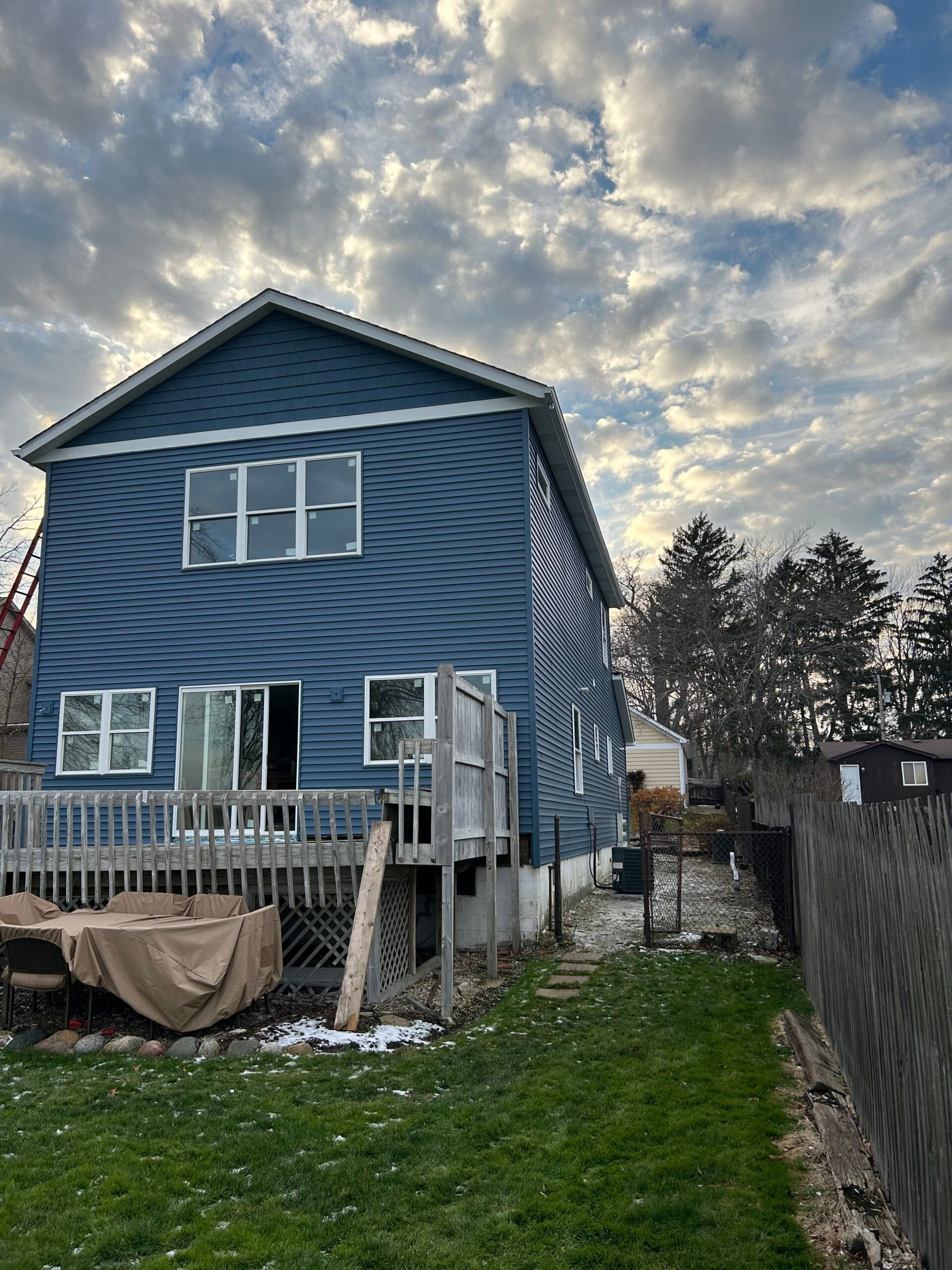 A blue house with a deck and a fence in front of it.