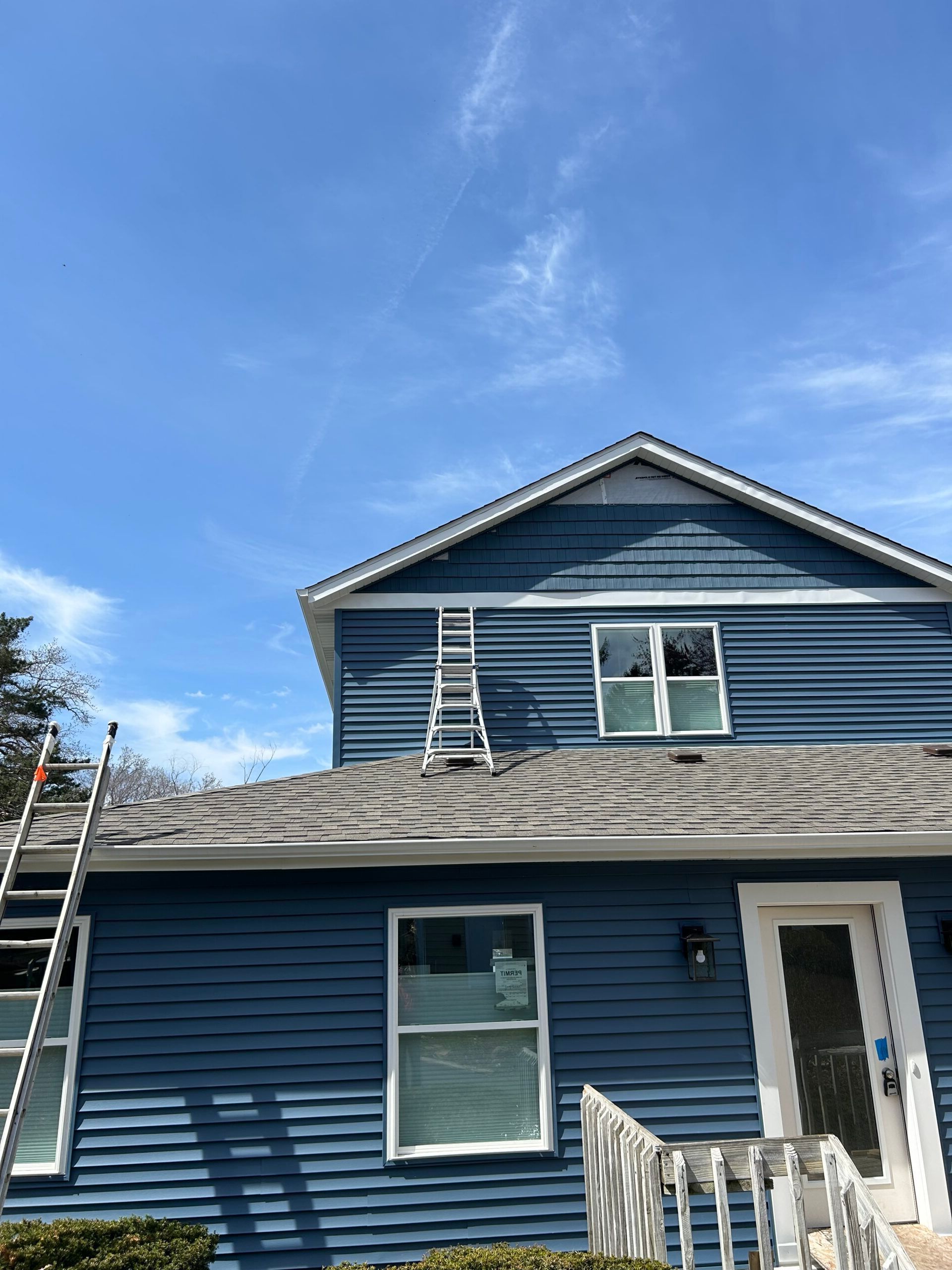 A blue house with a ladder on the roof is being painted.