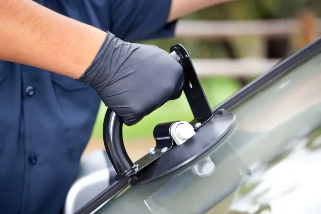 Una mano guantata utilizza una ventosa blu per installare o rimuovere il parabrezza di un'auto.
