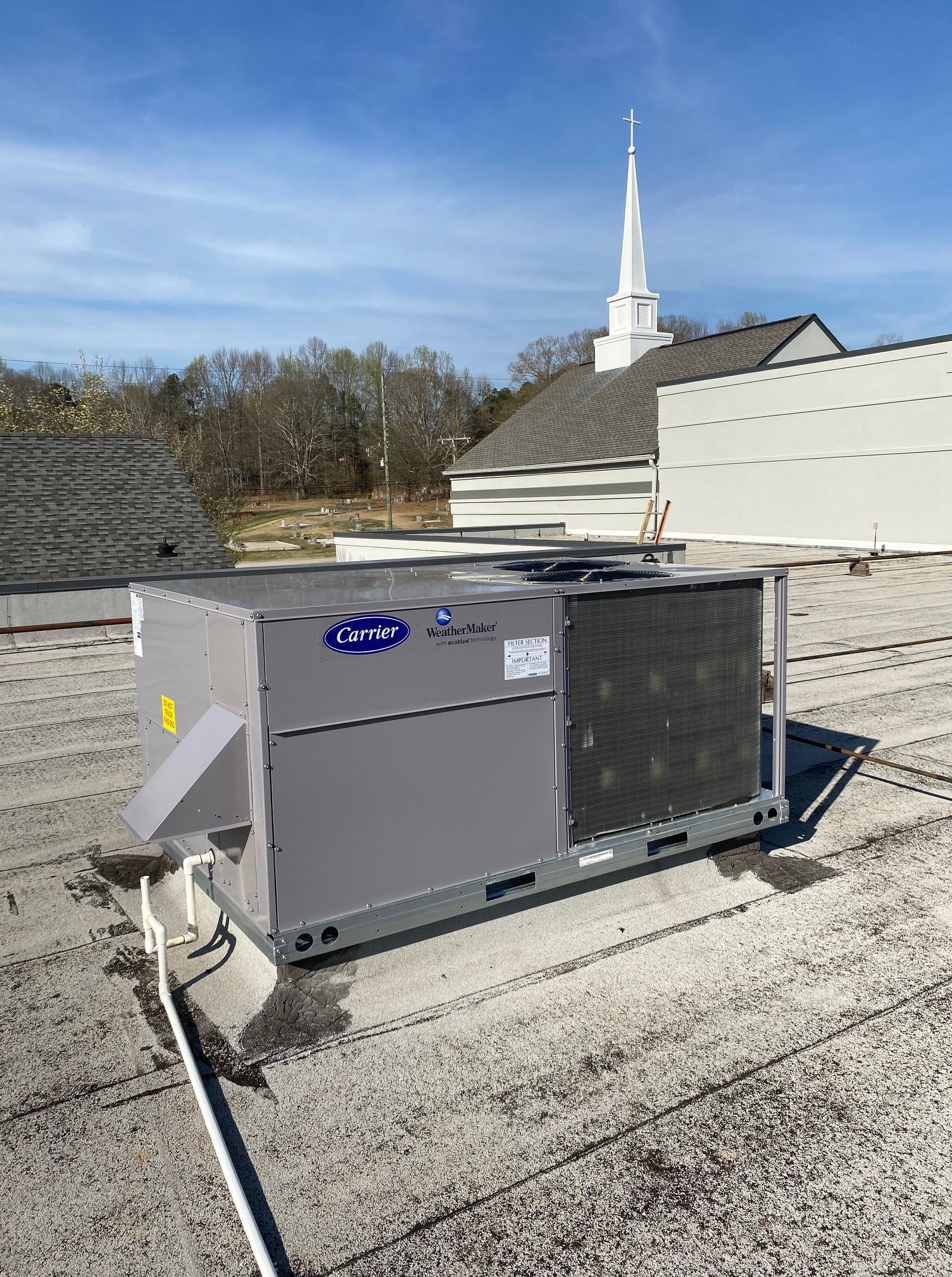 A large air conditioner is sitting on top of a roof next to a church.