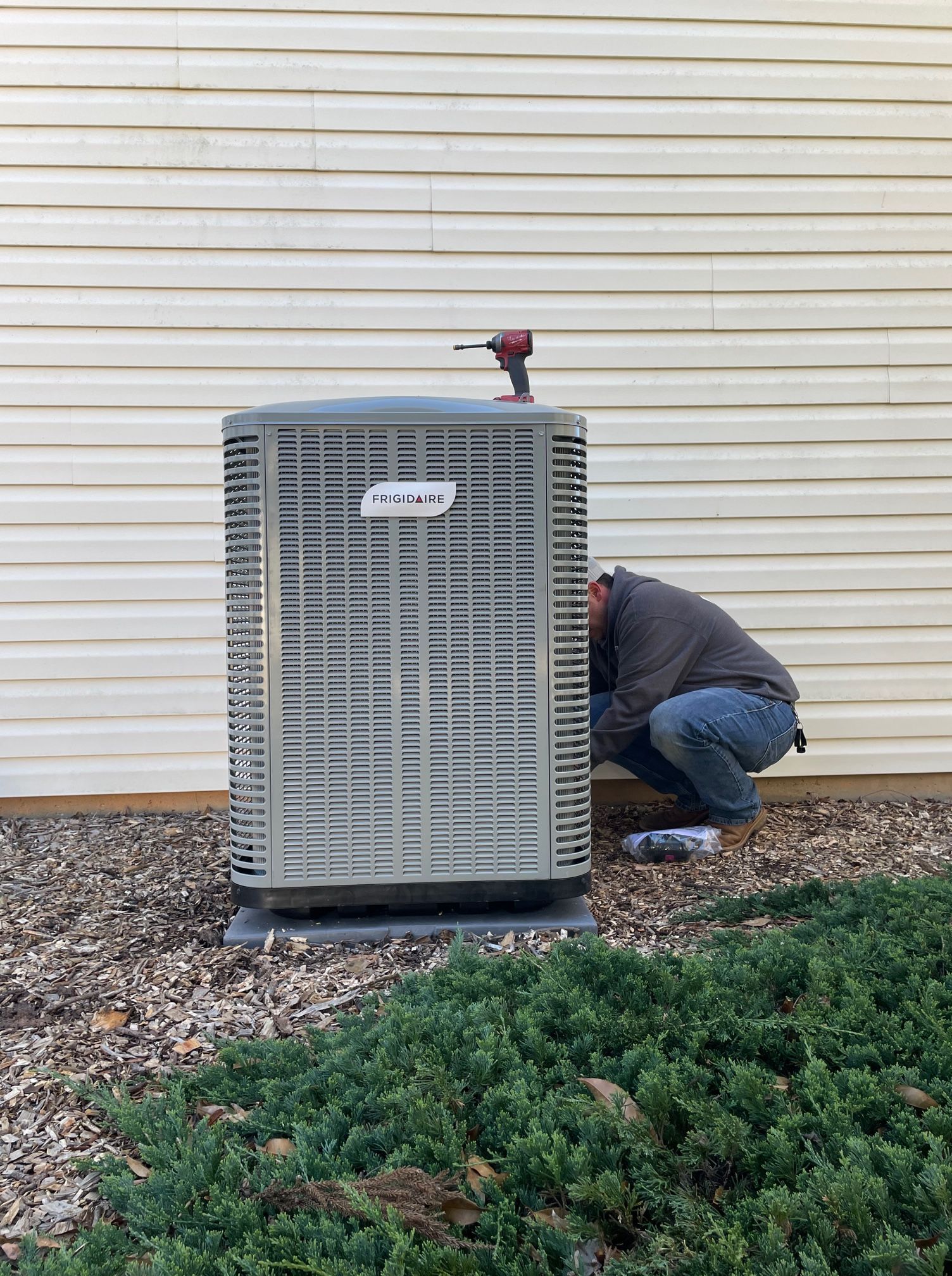 A man is working on an air conditioner outside of a house.