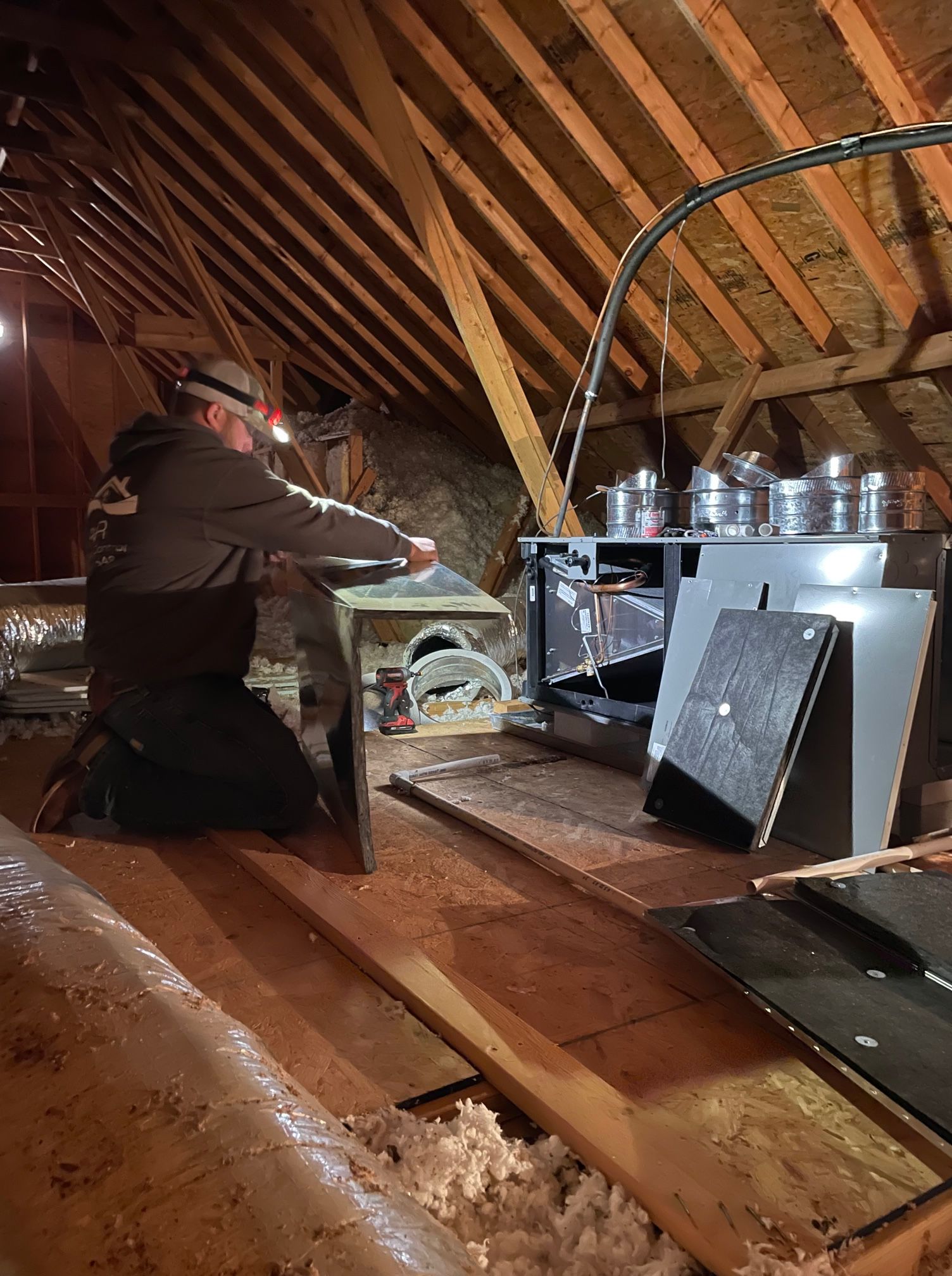 A man is kneeling down in an attic working on a machine.