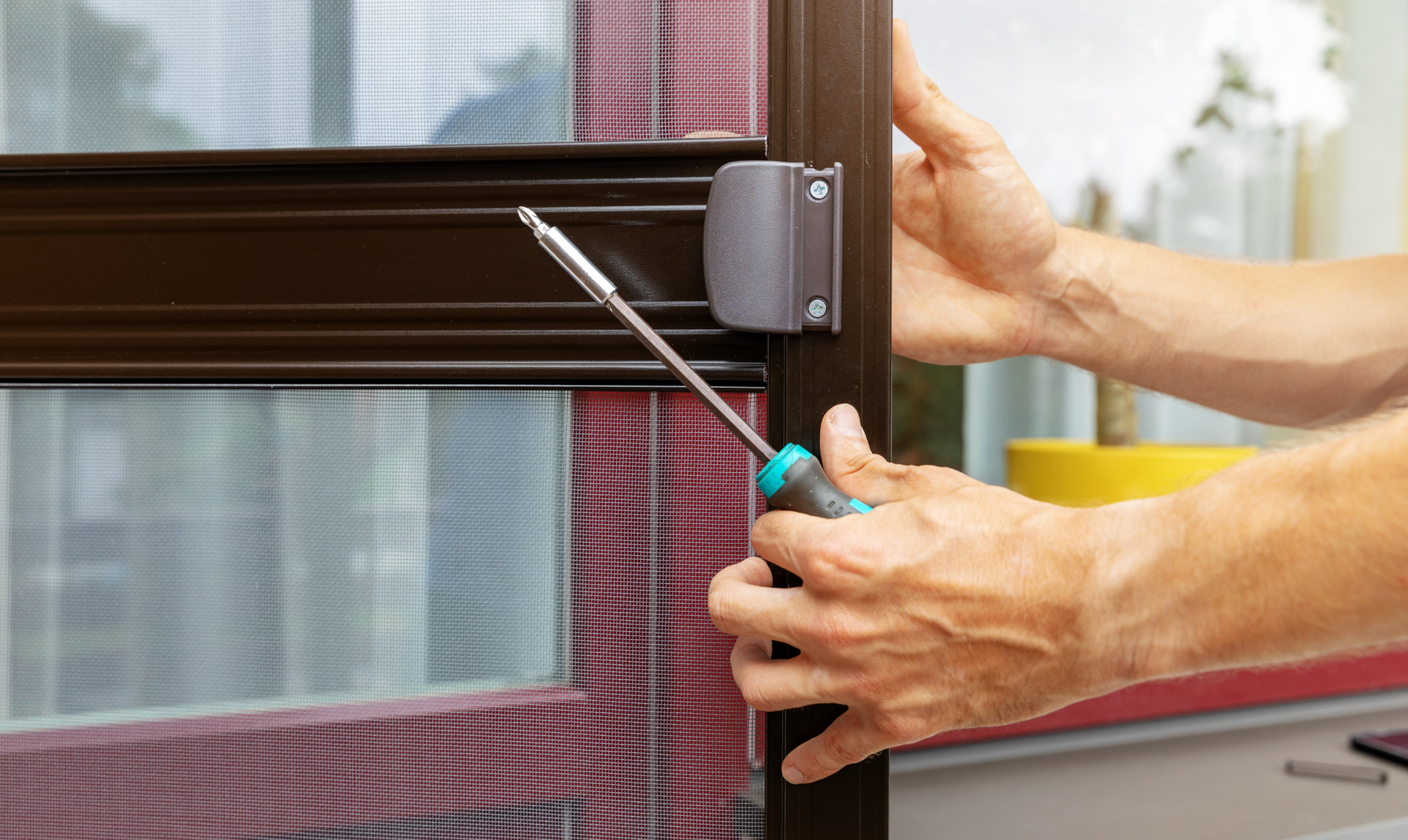 A person is fixing a screen door with a screwdriver.
