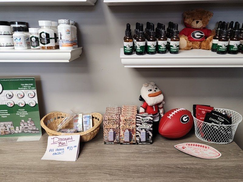 Shelves with health products and a teddy bear, along with a table featuring a football, a snowman, and various items for sale.