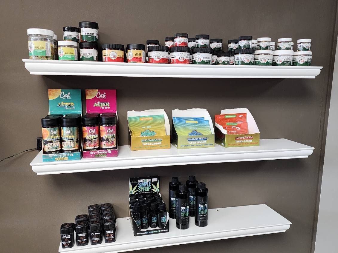 Shelves displaying various cannabis products, including jars and vape cartridges, in a retail setting.