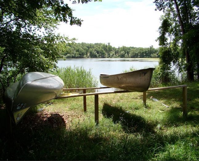 Two canoes sit on a wooden railing near a lake – Oxford, MI - Camp Oakland