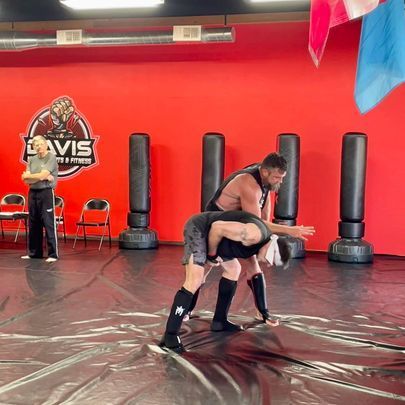 Two men are wrestling on a mat in a gym.