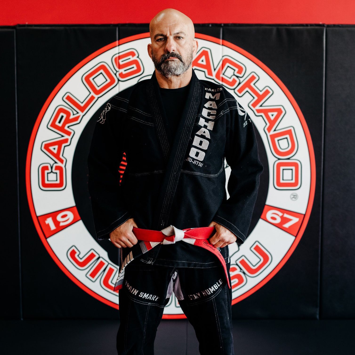 A man is standing in front of a sign that says carlos achado jiu jitsu