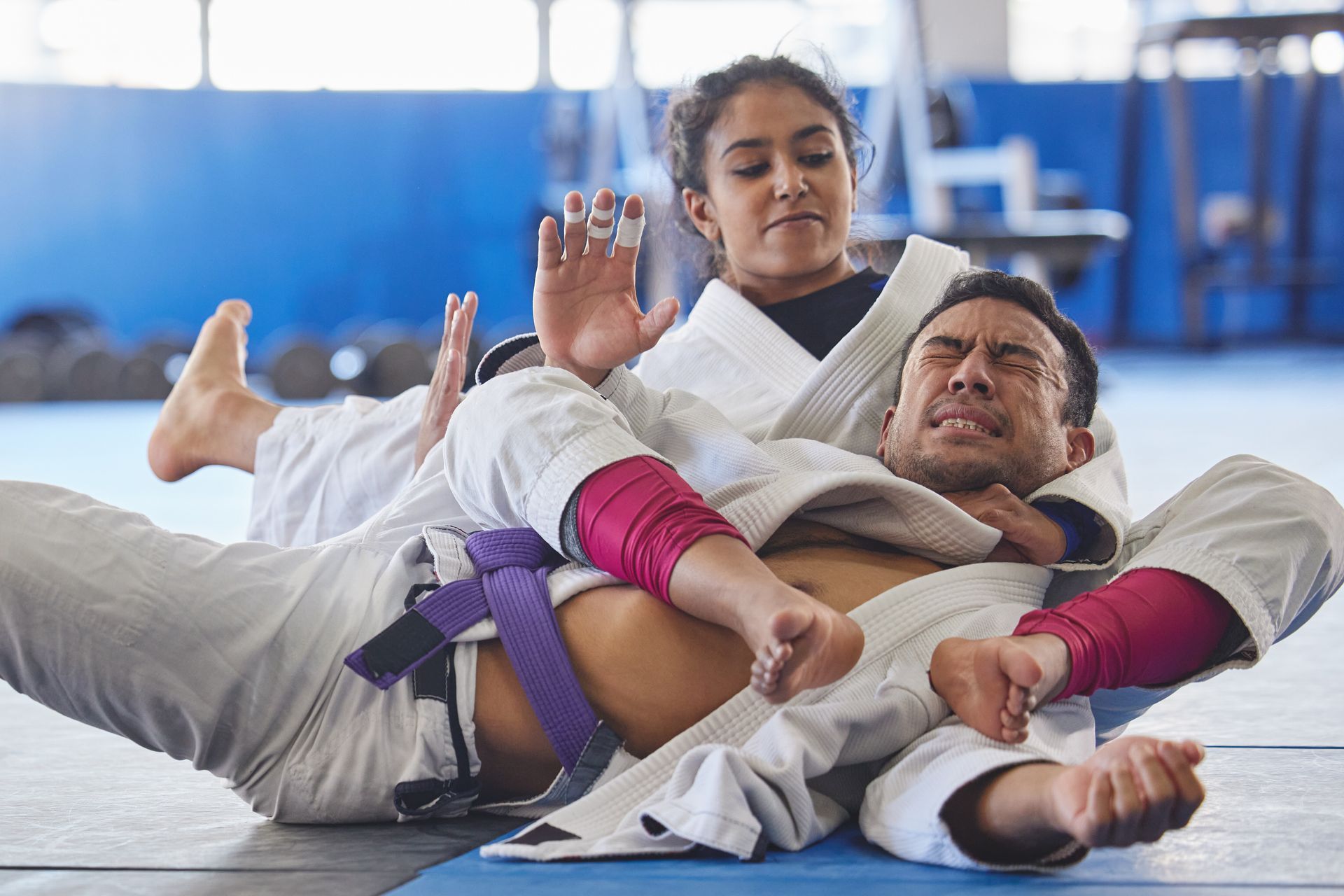 A man and a woman are wrestling on a mat in a gym.