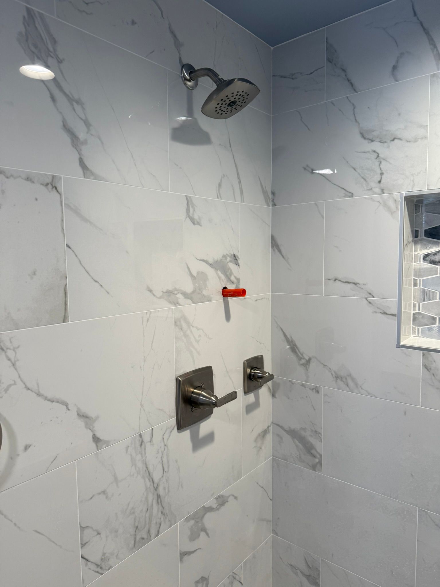 A shower with marble tiles and a red handle Bathroom Remodeling Company New Orleans