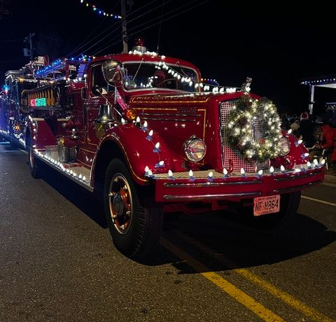 A red fire truck decorated with white lights and a wreath in a night parade in Cape May NJ
