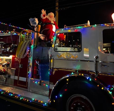 Santa Claus waves from a decorated fire truck at night, strung with colorful lights in Cape May NJ