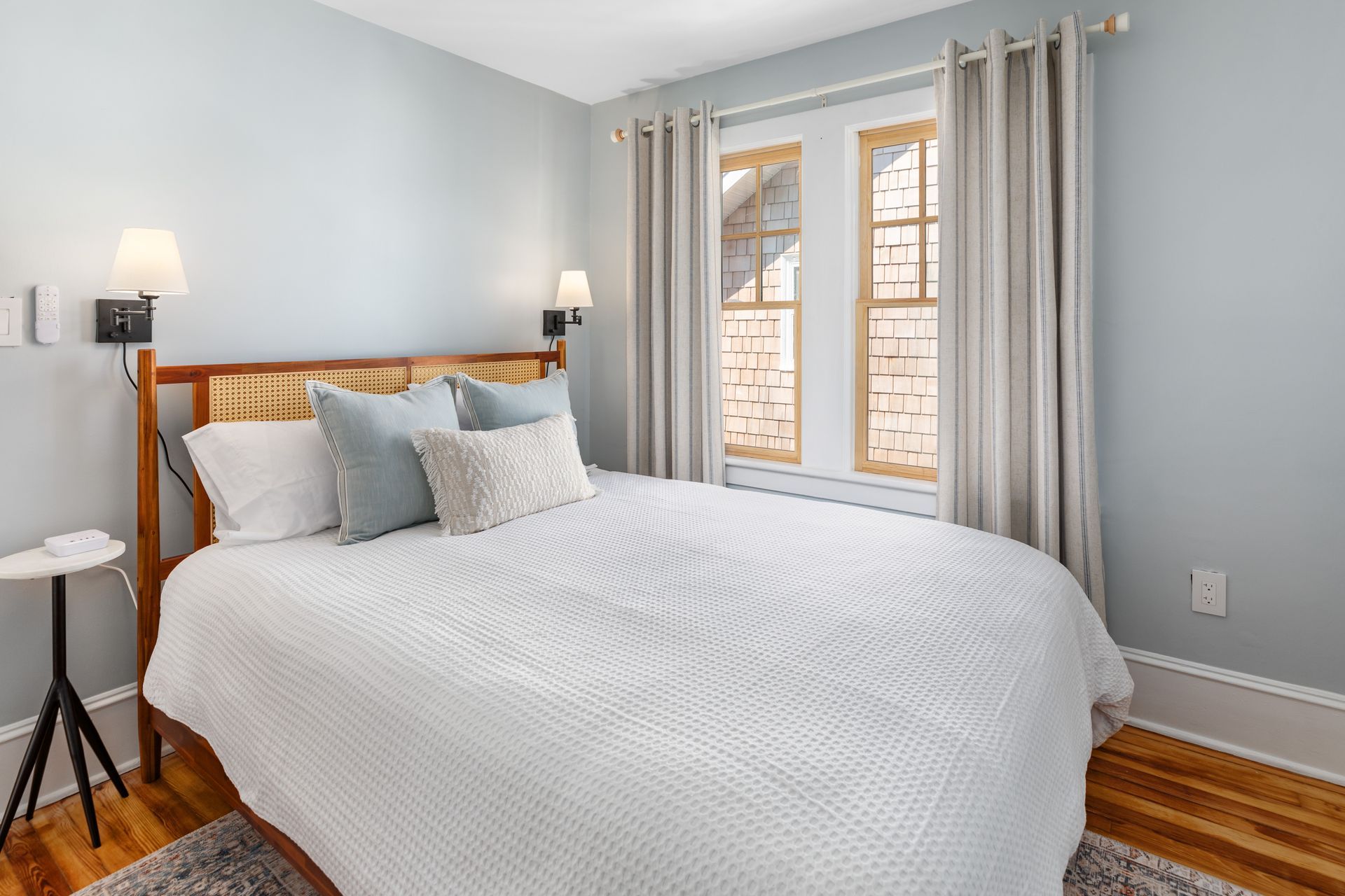 A bedroom with a bed , two windows and a nightstand.