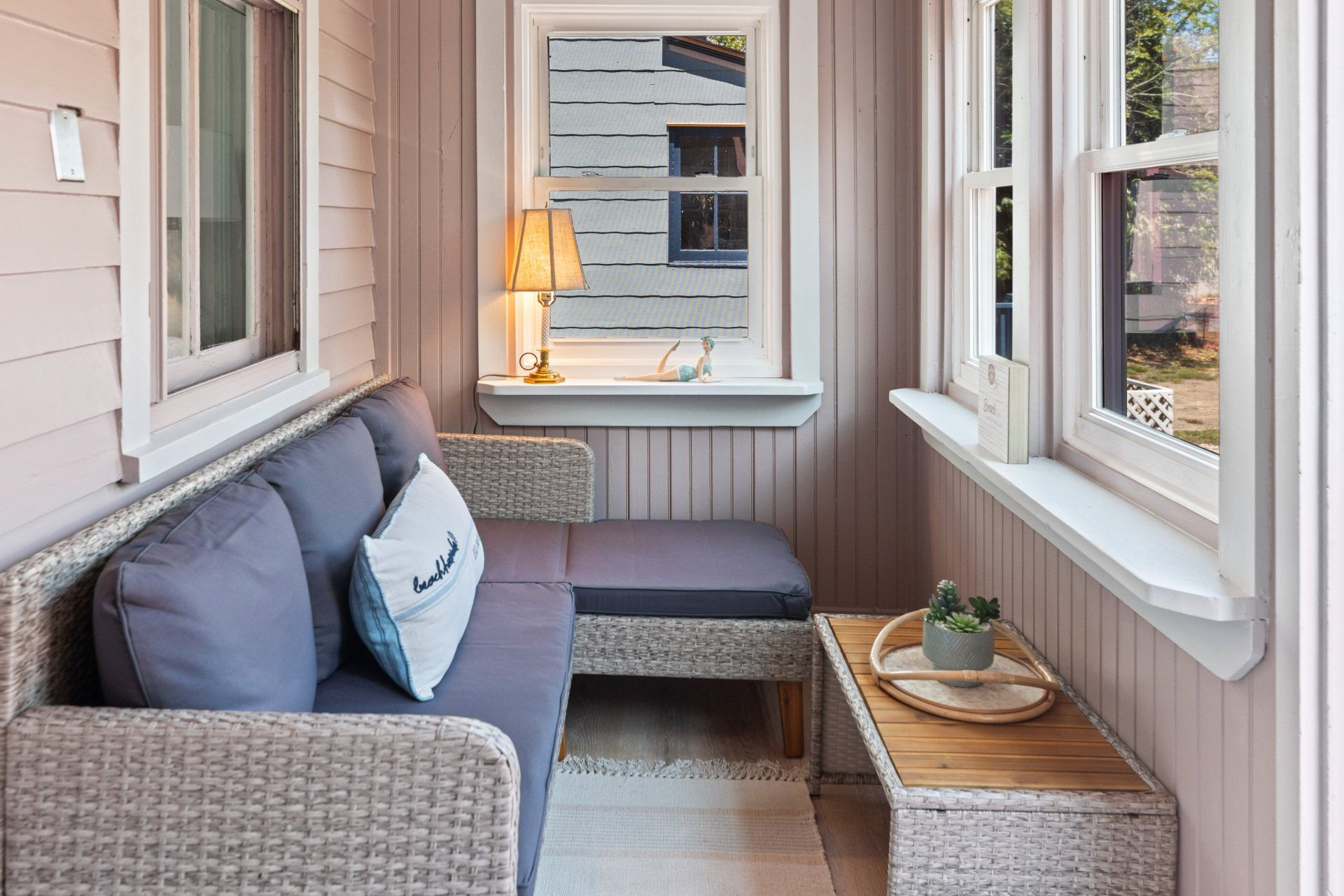 A small porch with a couch , ottoman , table and window.