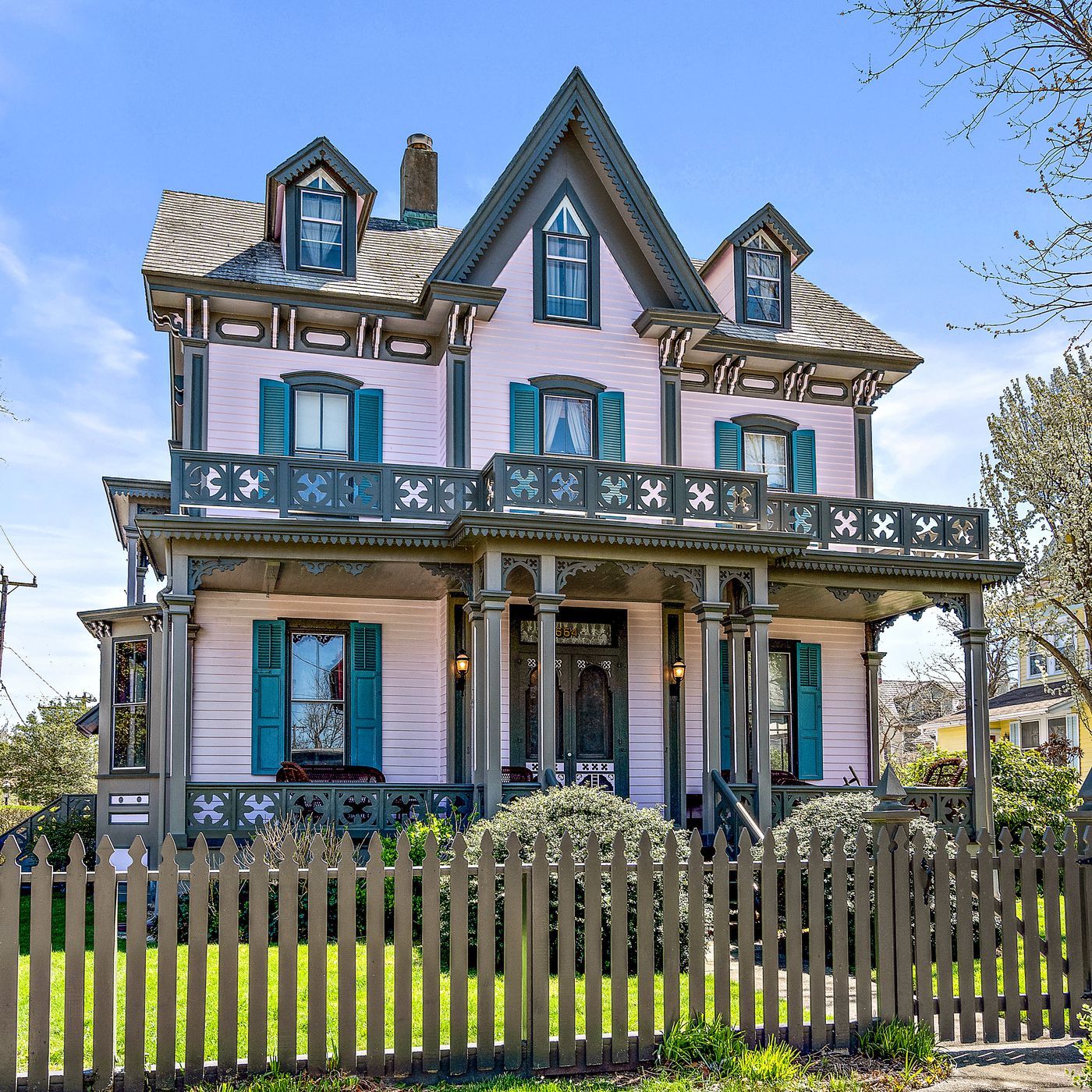 A large pink house with green shutters and a wooden picket fence
