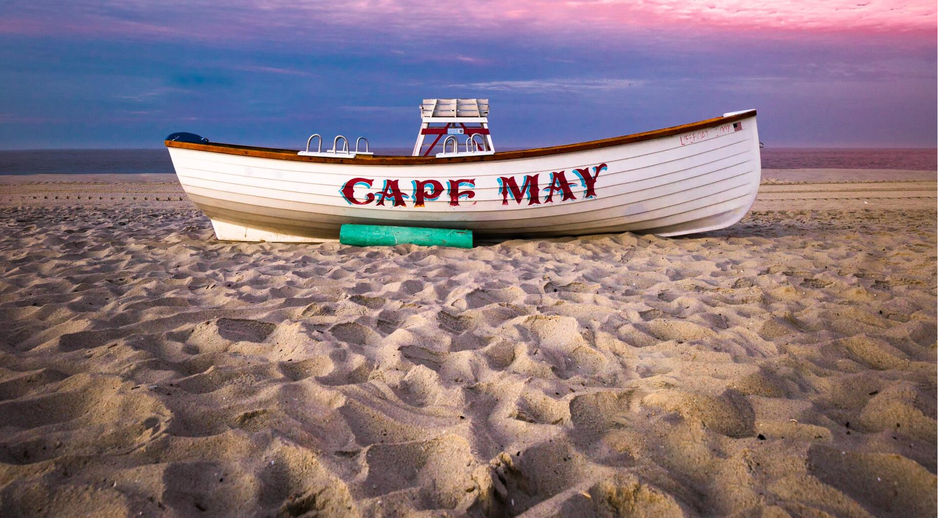 A boat named cape may is sitting on a sandy beach.