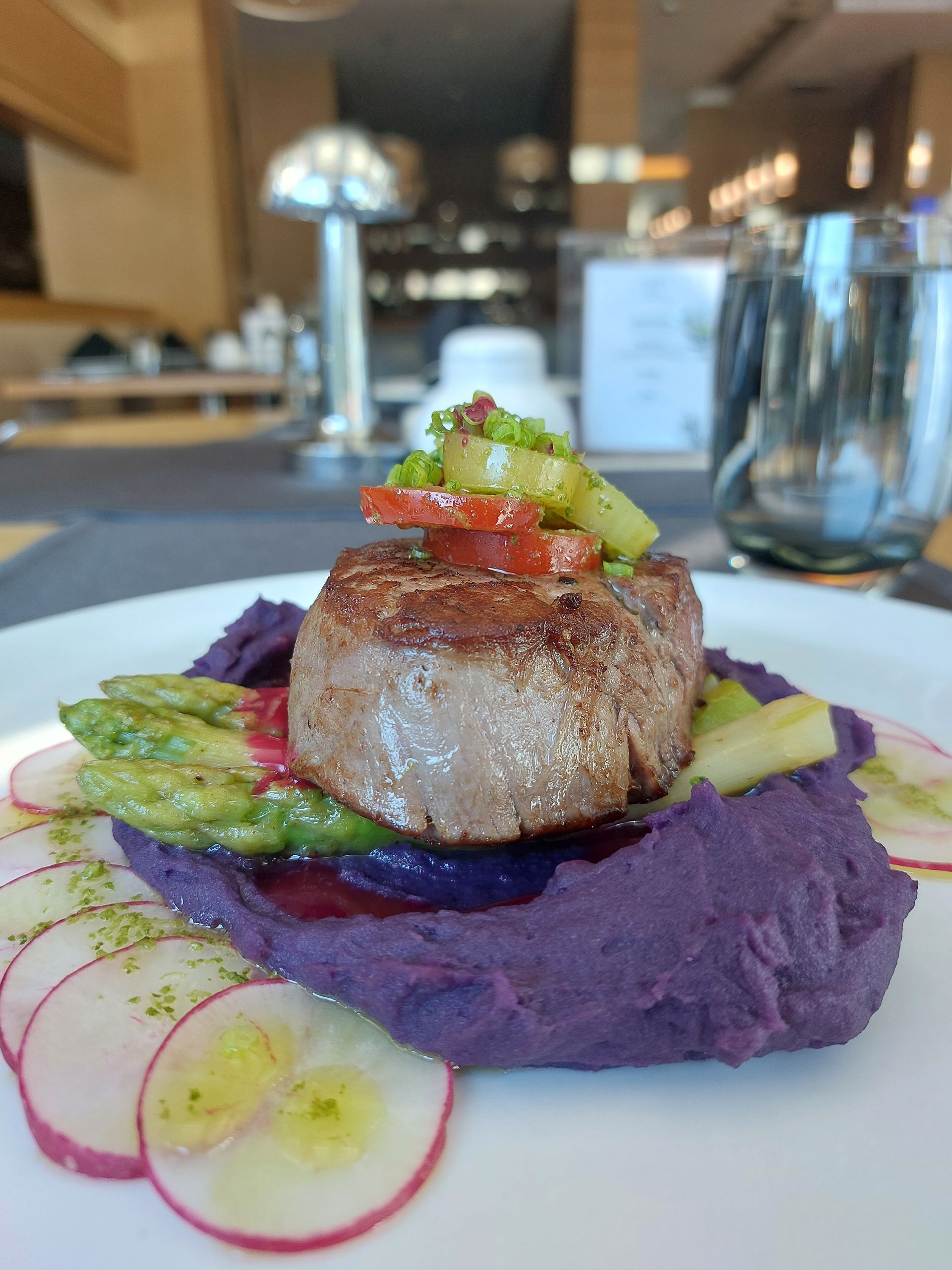 A plate of food with meat , mashed potatoes , asparagus and radishes on a table.