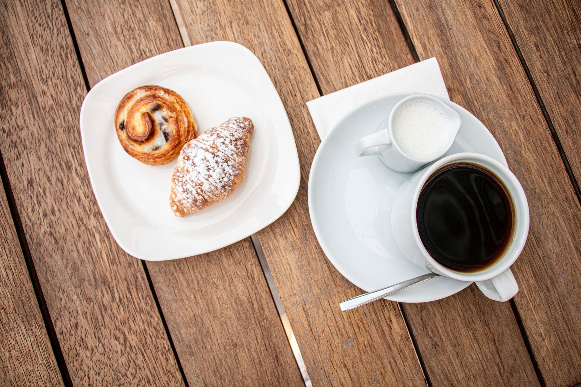 A cup of coffee and a plate of pastries on a wooden table.