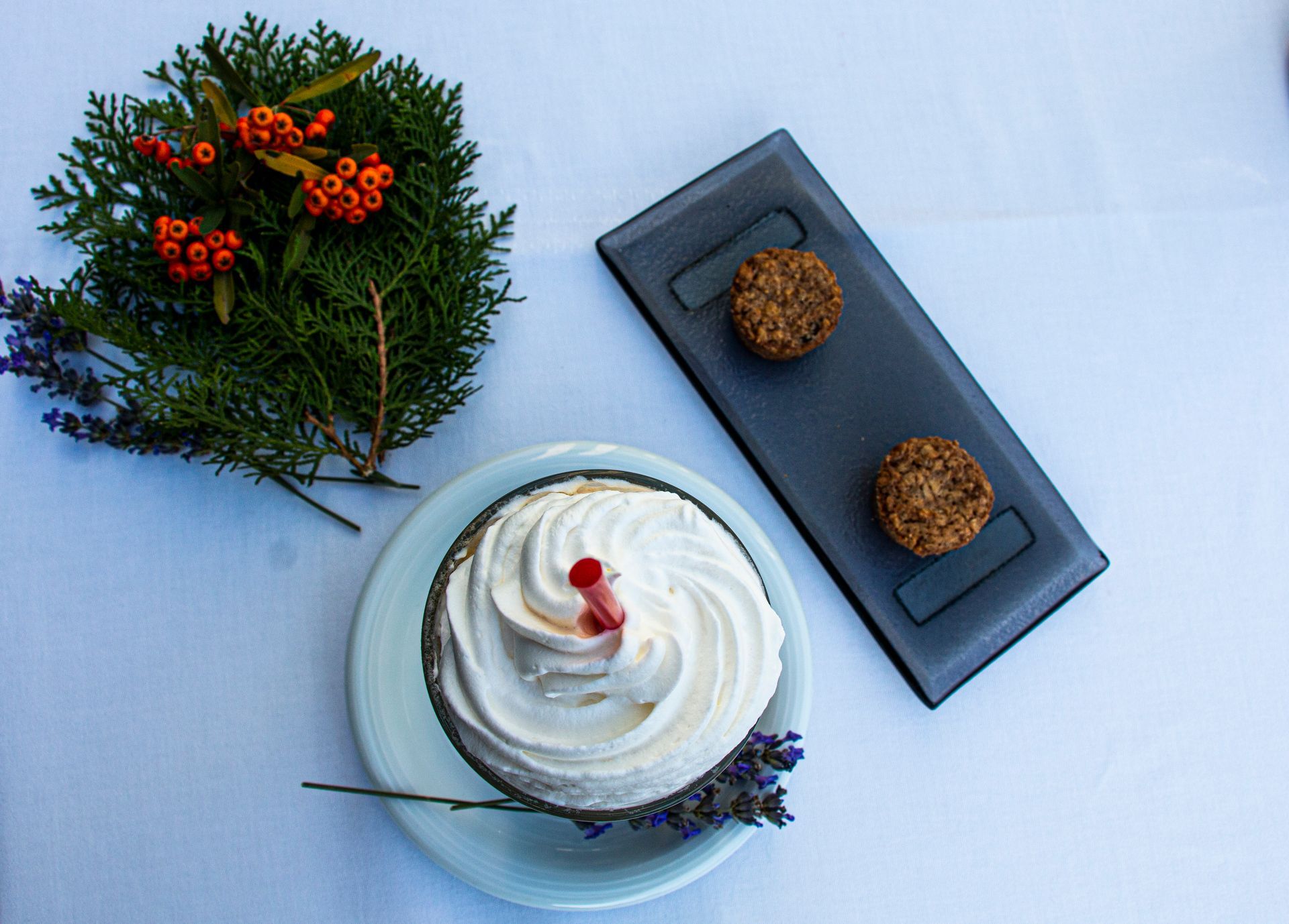 A dessert with whipped cream and berries on a plate next to a tray of cookies.
