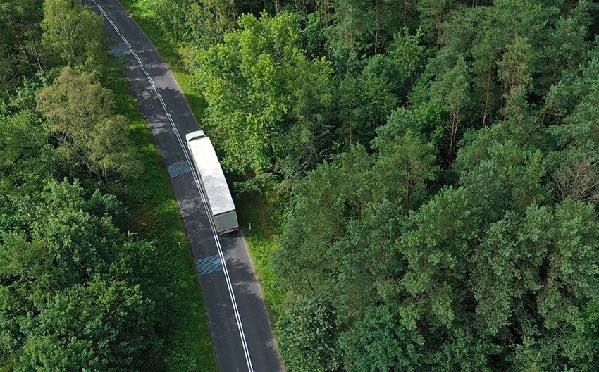 An aerial view of a truck driving down a road surrounded by trees.