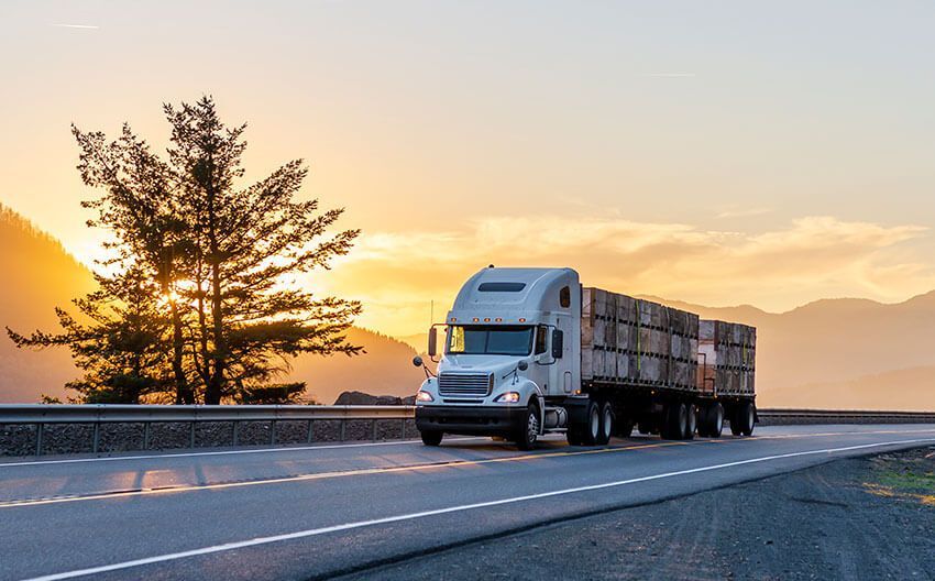 A semi truck is driving down a highway at sunset.