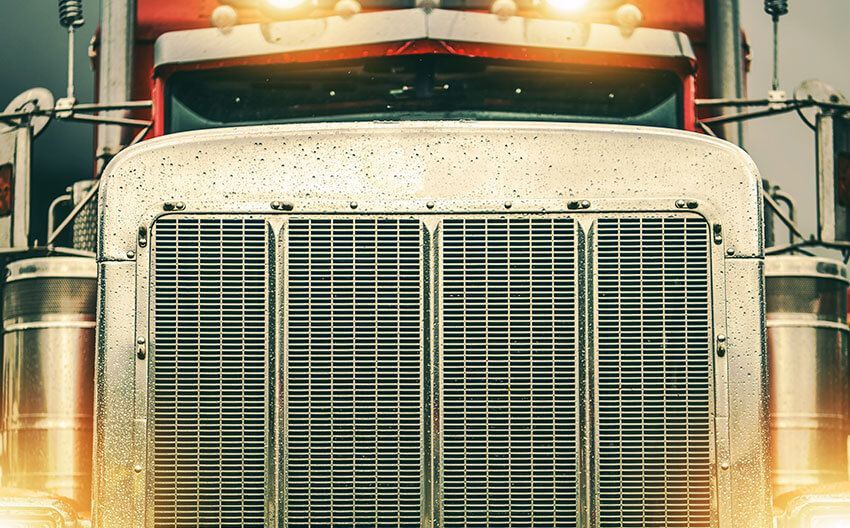 A close up of the front of a semi truck with its lights on.