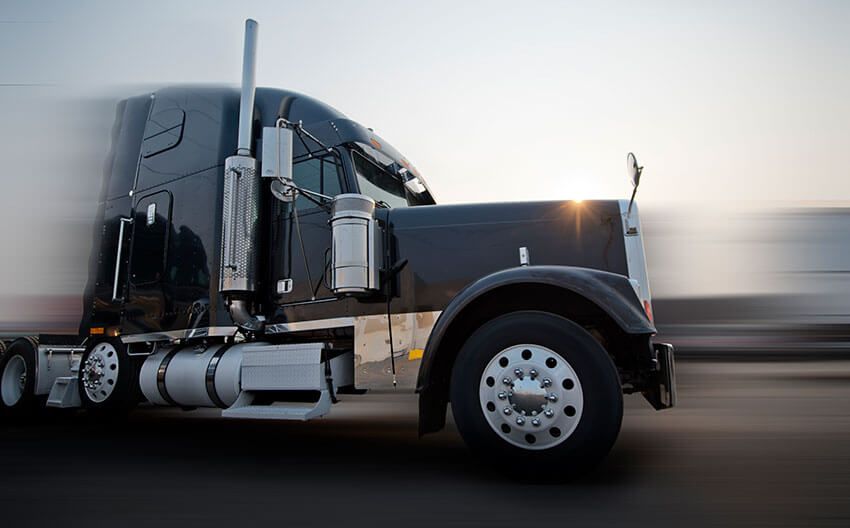 A black semi truck is driving down a highway.